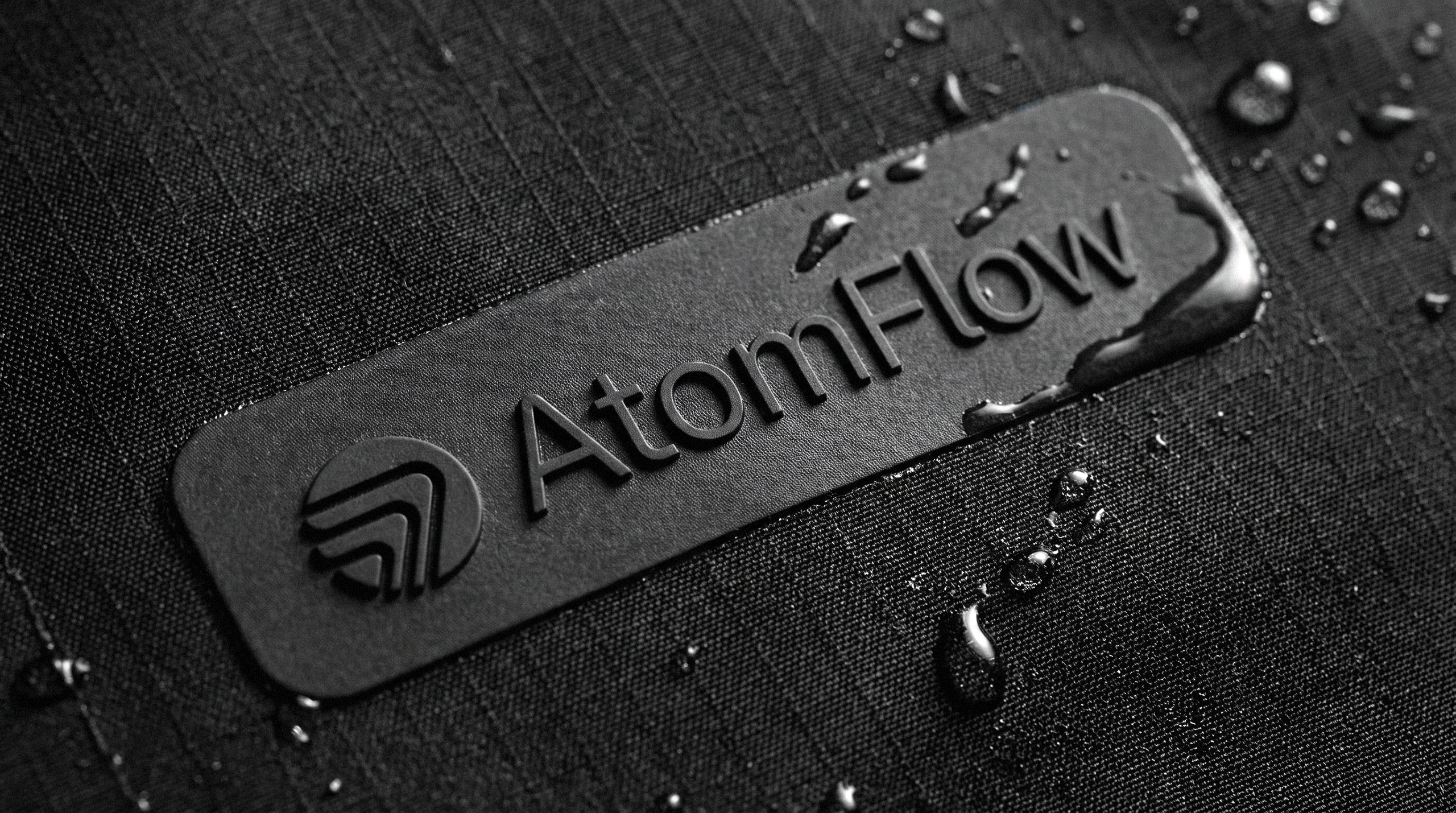 AtomFlow logo embossed on a dark, wet, textured waterproof material.