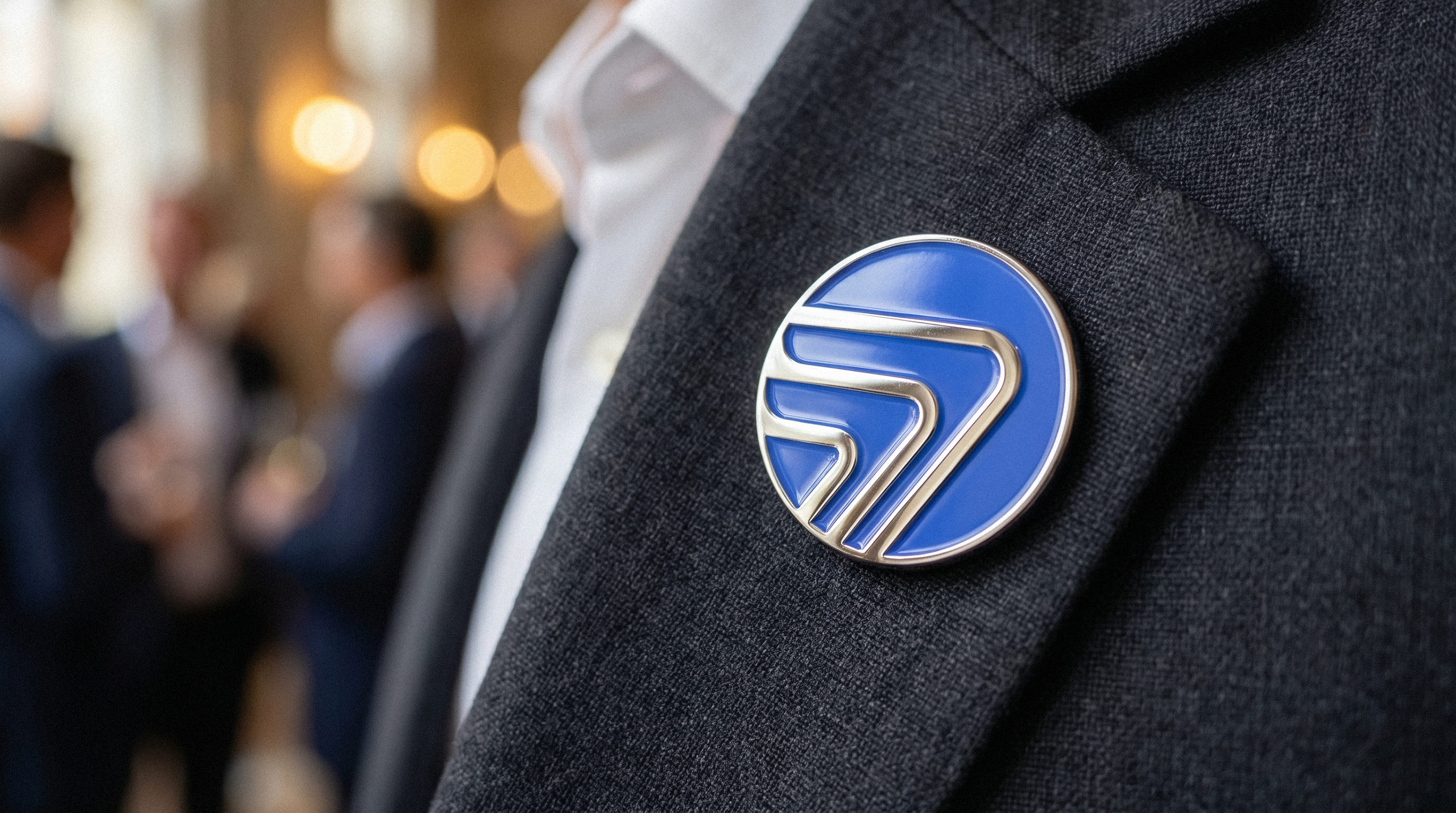 AtomFlow geometric logo as an enamel lapel pin on a grey suit jacket.