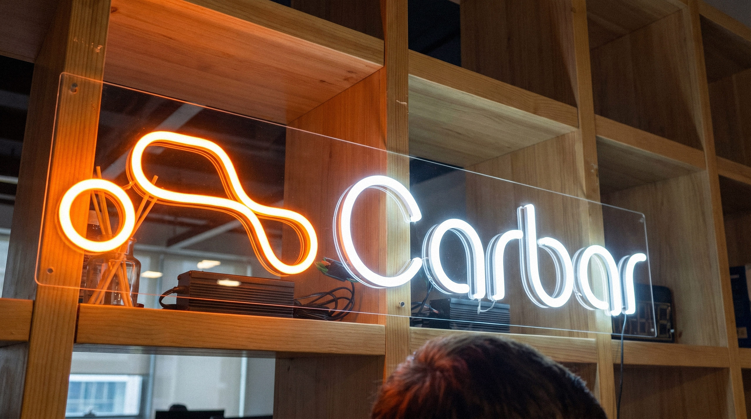 Bright neon light sign of the Carbar logo displayed on a wooden shelf - design by Brandforma Studio.