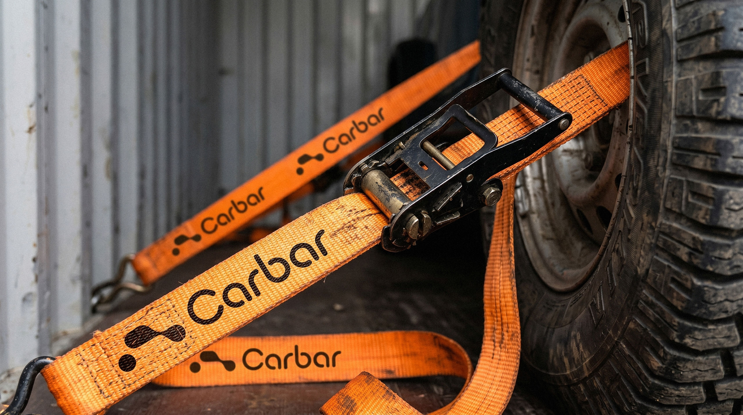 Orange industrial cargo ratchet straps printed with the black Carbar logotype securing a vehicle wheel - design by Brandforma Studio.