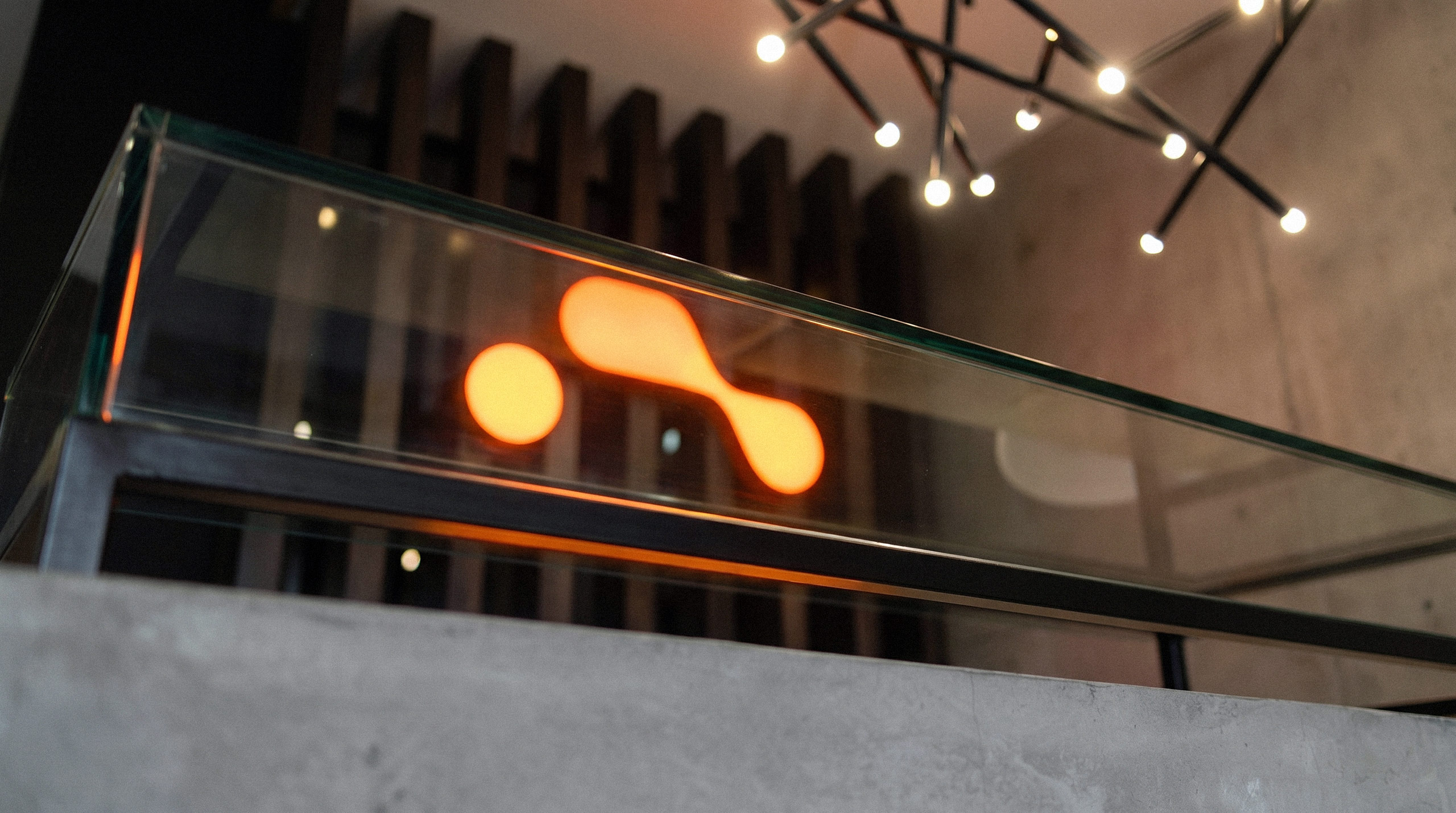 Glowing orange Carbar logomark embedded in a modern glass and concrete reception desk - design by Brandforma Studio.