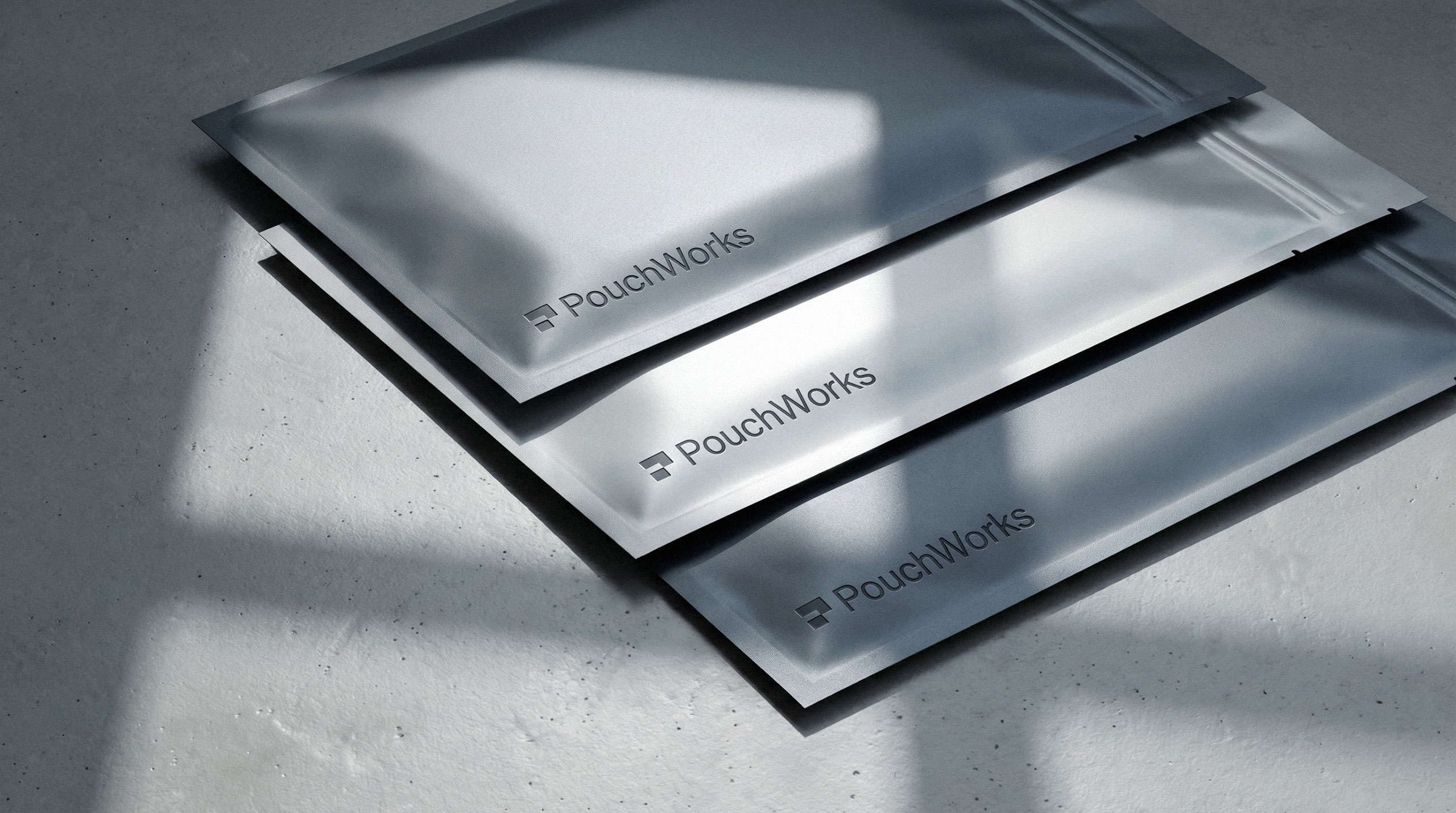 Stack of three flat silver foil packaging pouches with embossed logo by Brandforma Studio