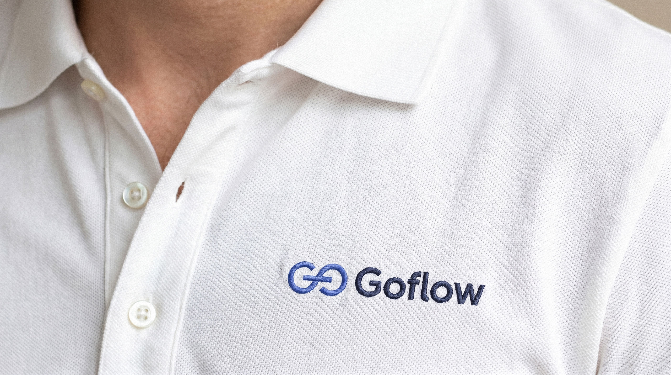 Close up of a white polo shirt embroidered with the dark blue Goflow logo