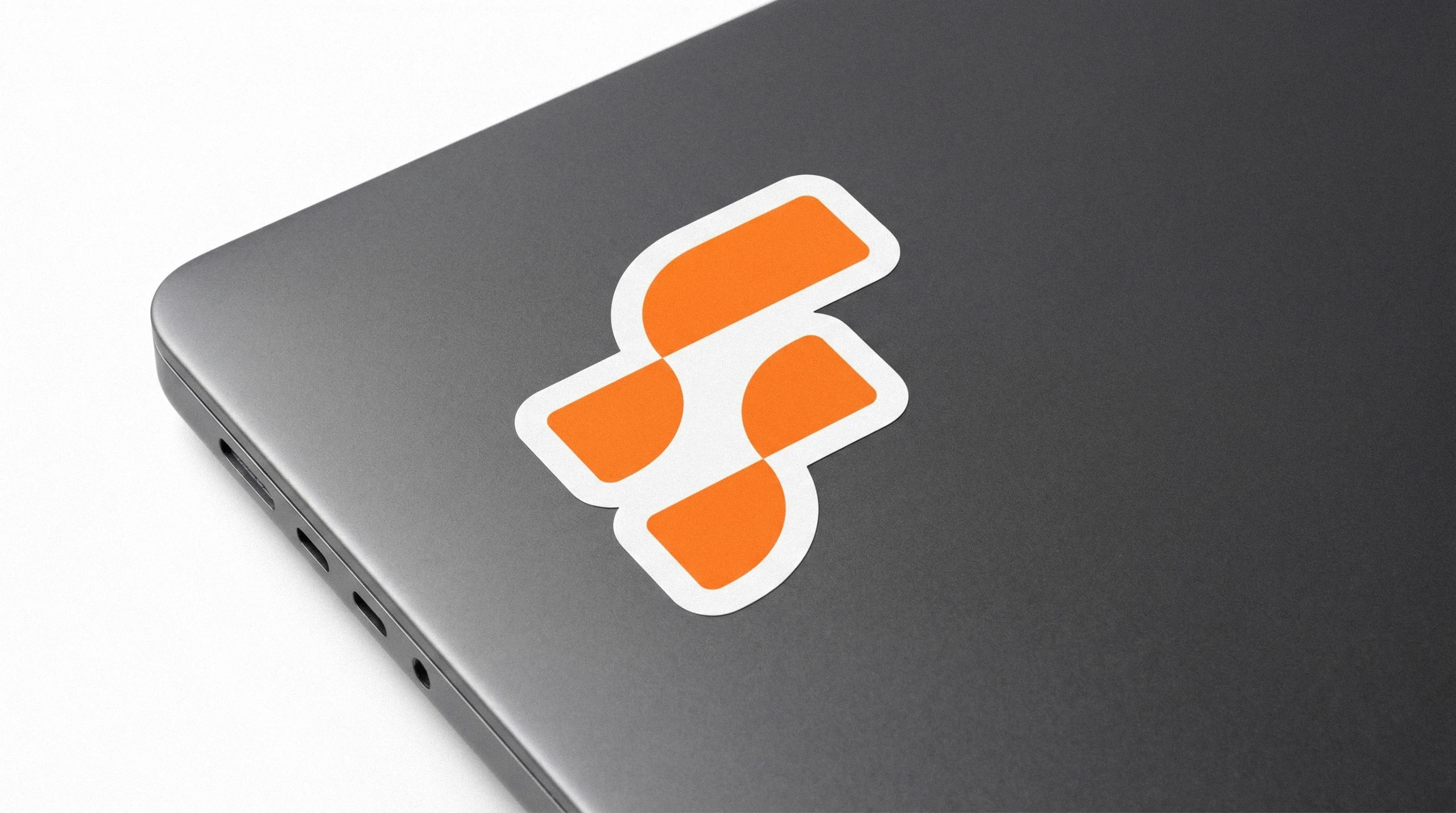 Orange FirstMotion F symbol as a die-cut sticker on the corner of a dark laptop
