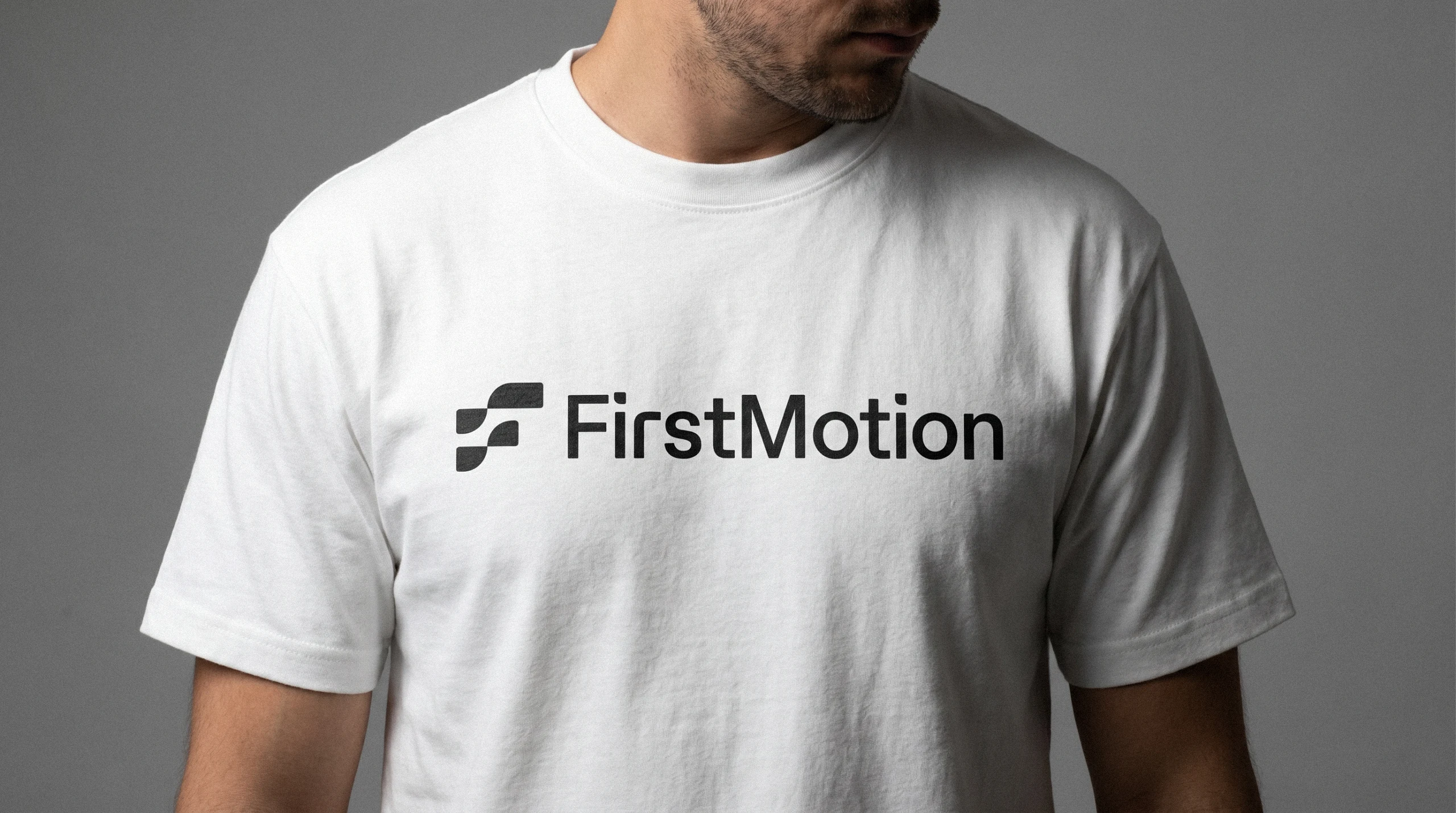 Person wearing a white FirstMotion t-shirt with the dark logo across the chest
