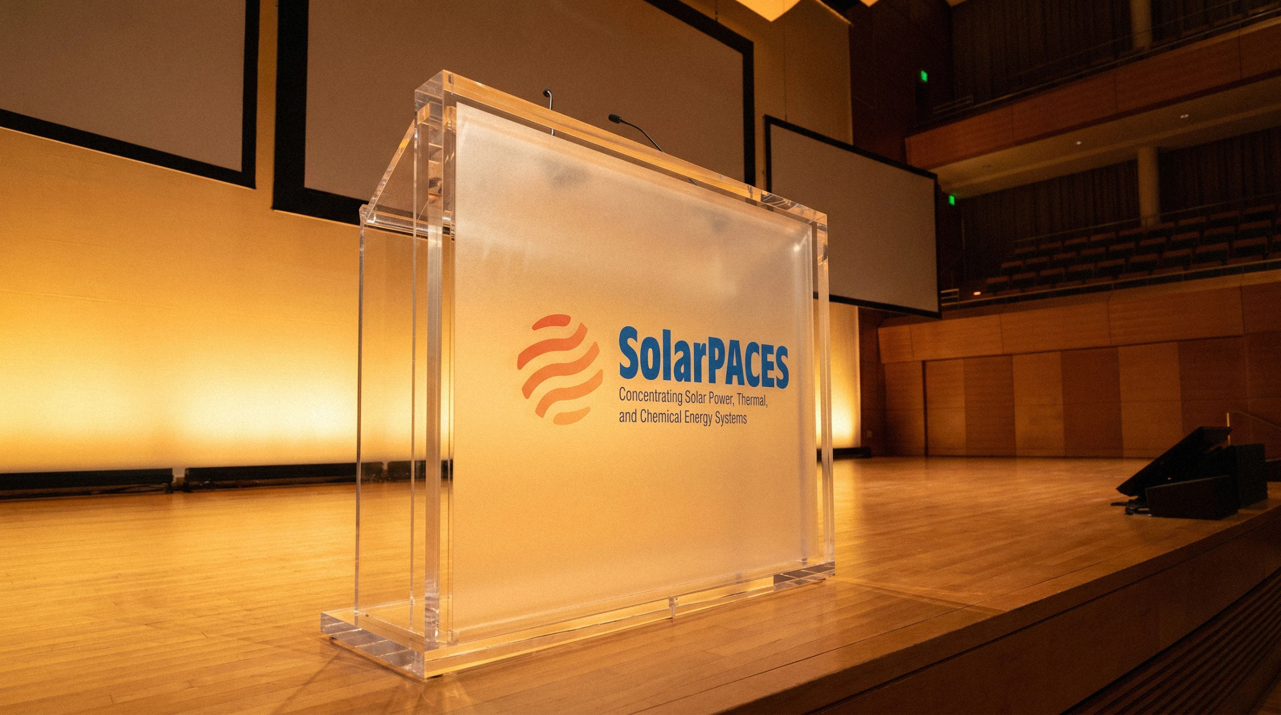 SolarPACES Acrylic Lectern – Stage Branding Clear acrylic SolarPACES lectern with the logo applied, lit on a conference stage