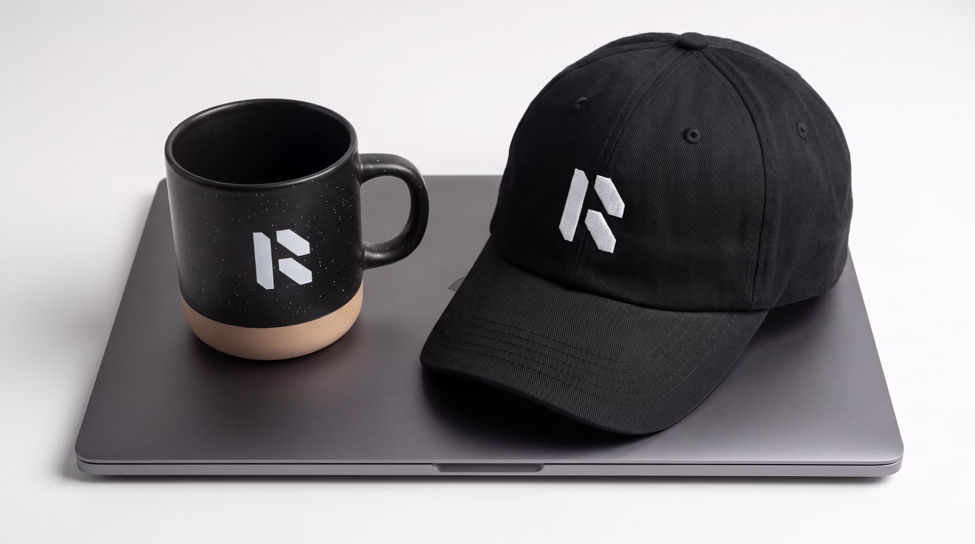 Modern Tech R logo displayed on a black coffee mug and a black baseball cap resting on a laptop.